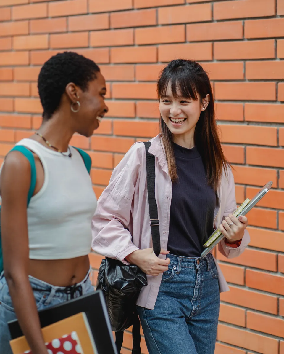 Two smiling students talking outdoors with their books