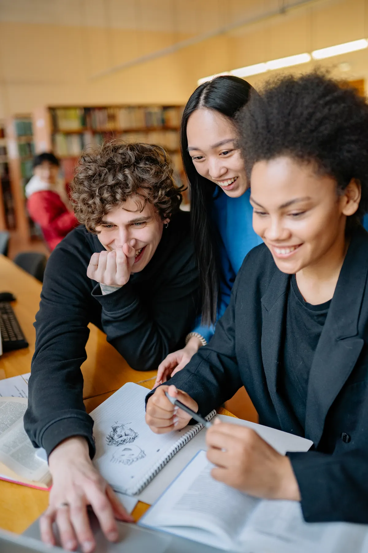 Three smiling students studying together in a library