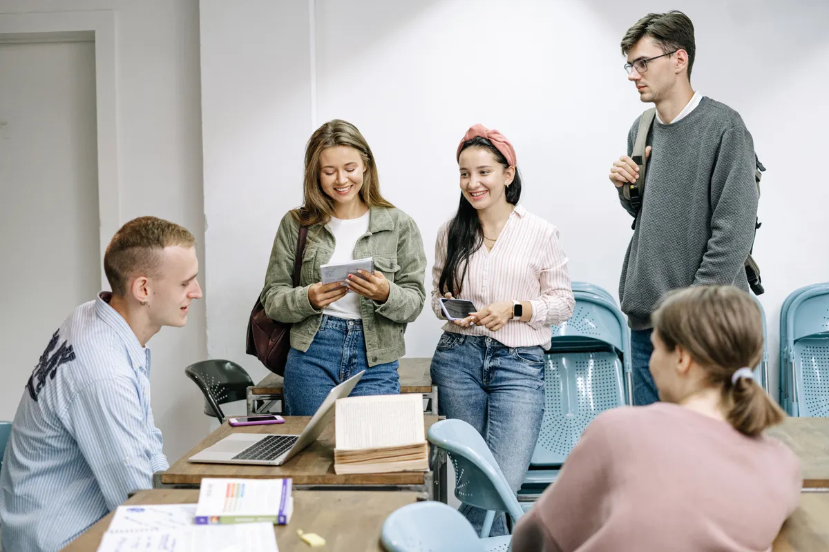 Students talking around a table with books and a laptop